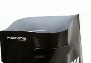 Γυαλιστερή πλαστική τσάντα με χούφτα και λογότυπο Xenos Packaging, ιδανική για καταστήματα μόδας ή eshop.